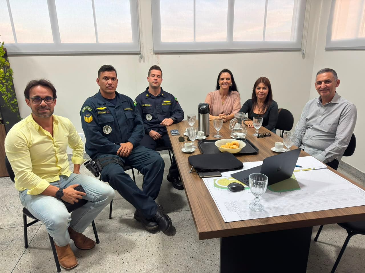 Reunião institucional em mesa de trabalho, com plantas do projeto sobre a mesa
